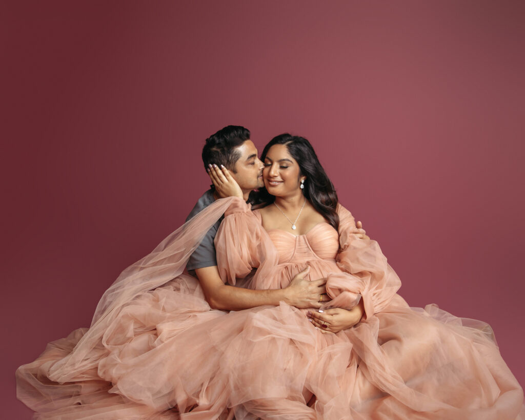 dad kissing mom maternity photo in light pink dress
