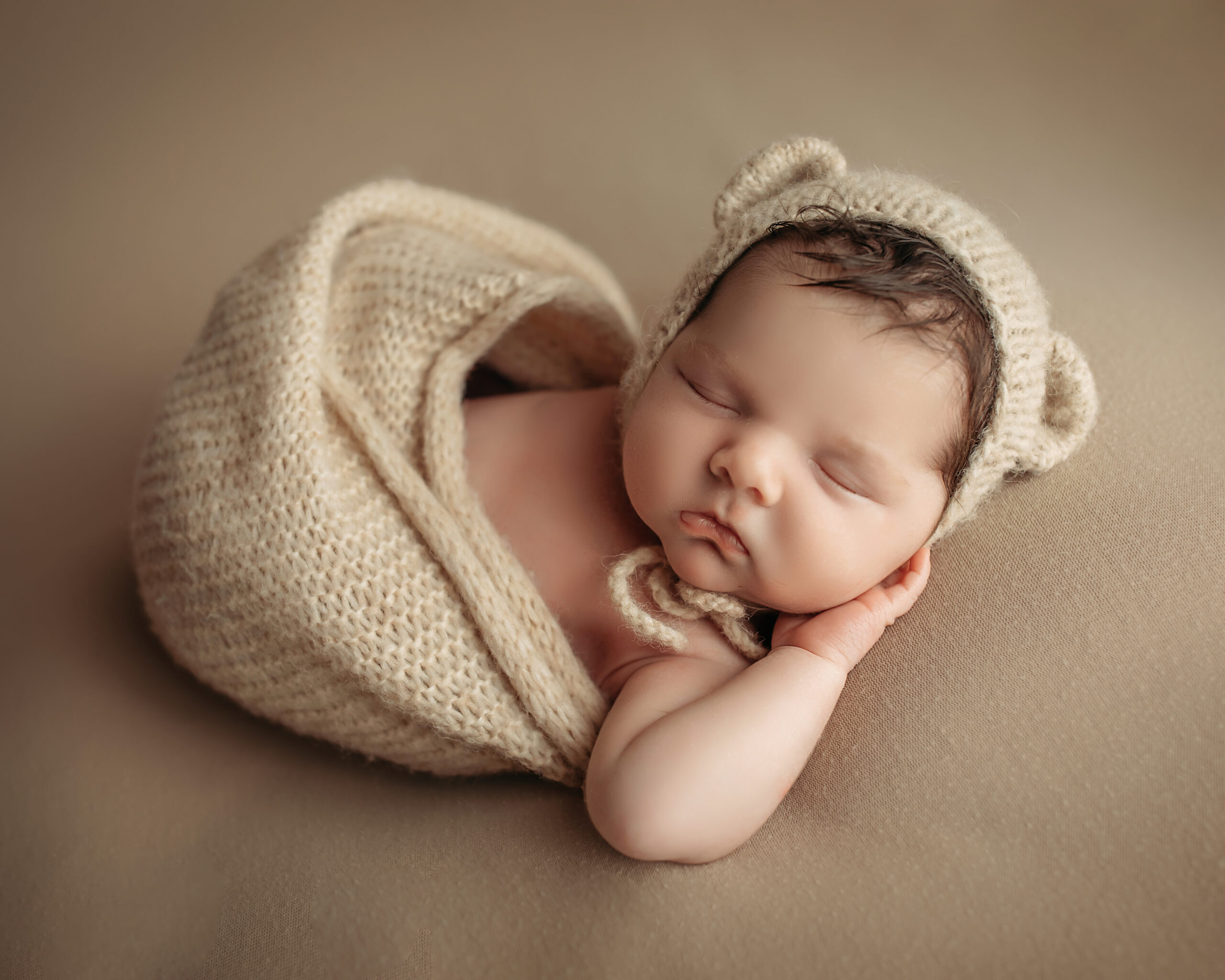 newborn baby wearing cream colors and bear ears bonnett with hand behind cheek