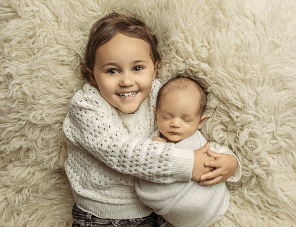 Smiling big sibling holding newborn baby during newborn photography session