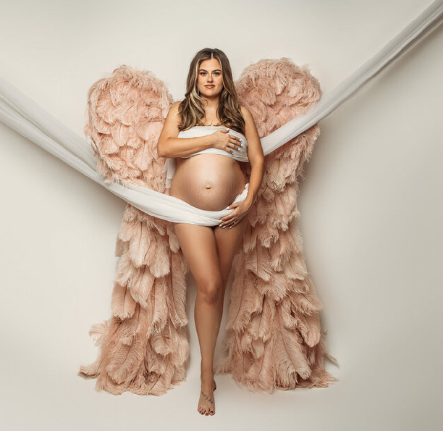 mother using draping and pink angel wings during her maternity session