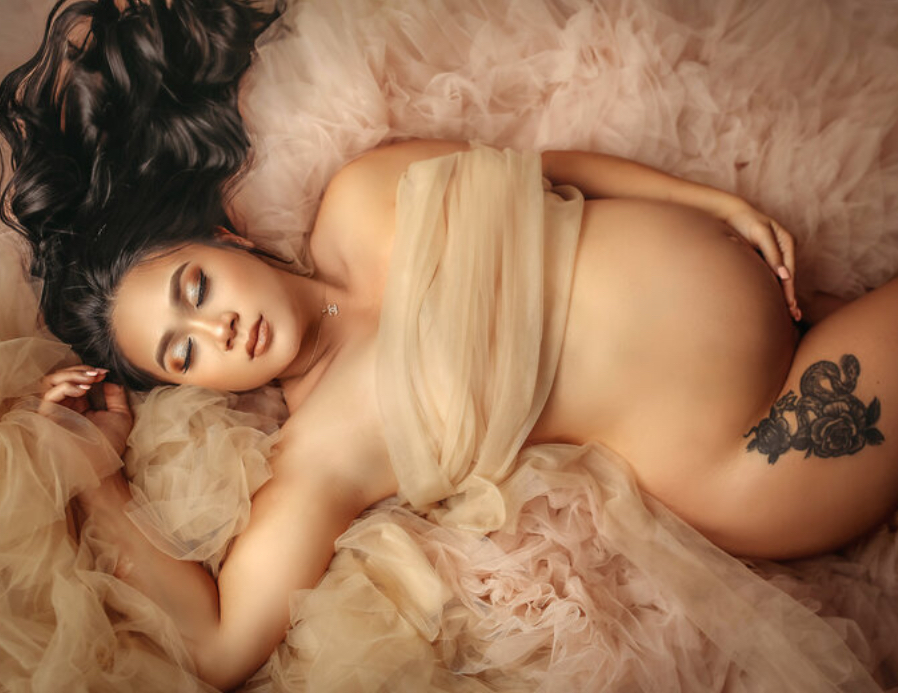 mother laying in fluffy blanket draped with beige draping in her OKC maternity photoshoot