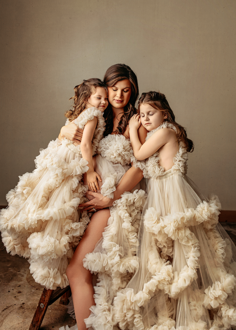 mother and daughters embracing baby bump in beige flowy dresses