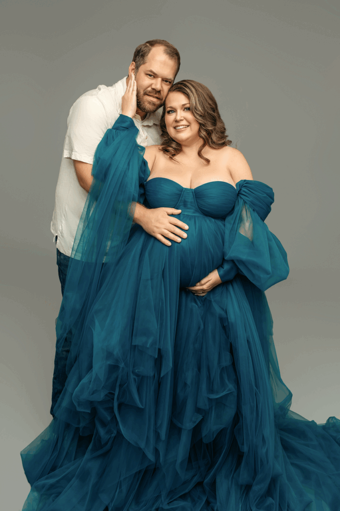 partners smiling holding belly bump while wearing blue gown