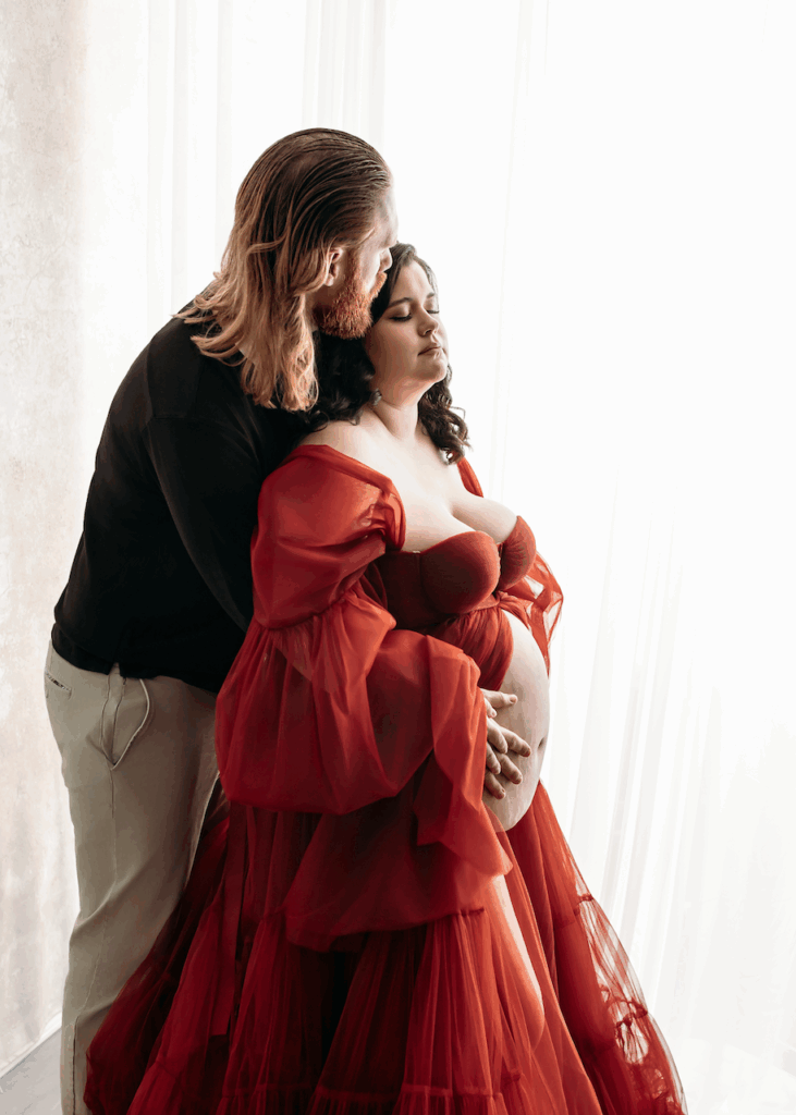 partner holding mothers belly whos in a red flowy gown