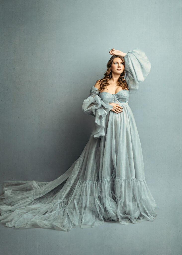 maternity shoot with light blue gown posing with hand on belly