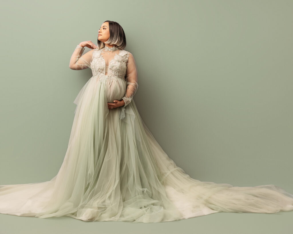 Indoor maternity photoshoot with pregnant mom in long-sleeved flowy sage colored gown.