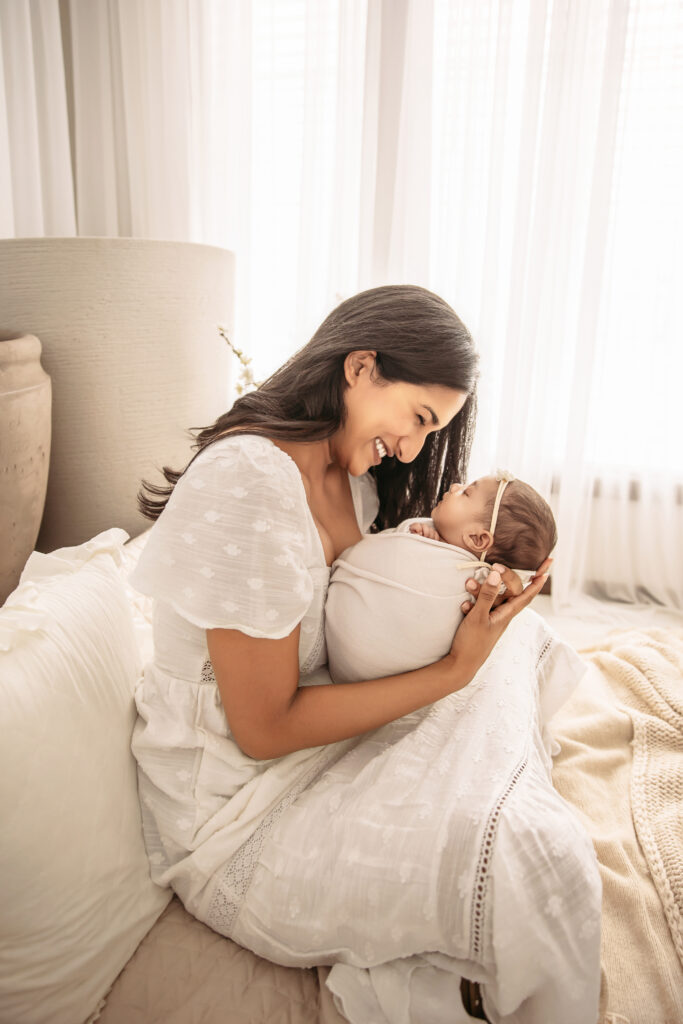 A sleeping baby swaddled in a cream wrap with mom for summer newborn photos by Oklahoma City photographer Ashley McClintock Photography.