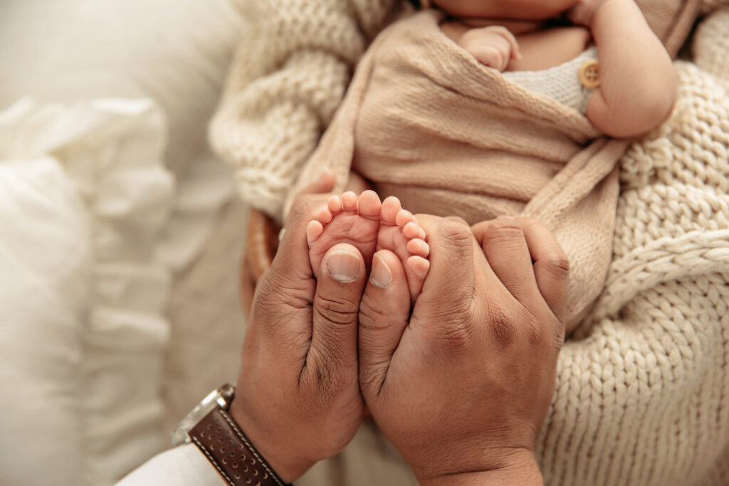 A close-up of a father gently holding his baby's tiny feet in a calm, climate-controlled studio for summer newborn photos by Ashley McClintock Photography.