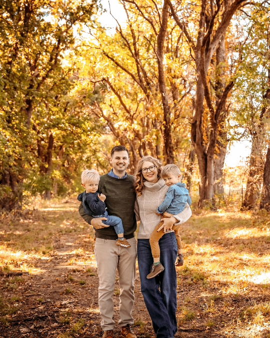 Family of four in autumn with golden leaves posing for fall family photos.