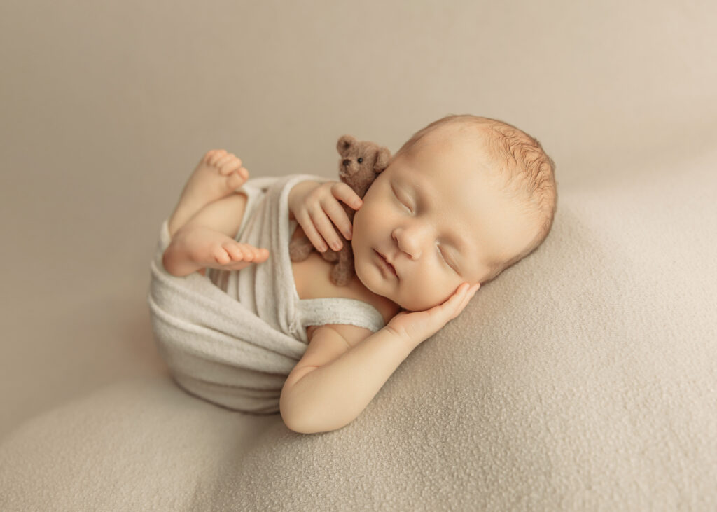 Baby in cream wrap with a little teddy bear during a photo session for newborn.